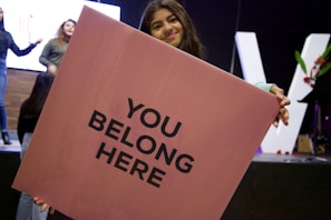 A smiling individual holding a sign that reads 'You Are Not Alone' at a community gathering.