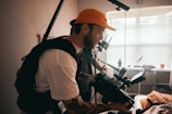 man in white shirt and orange cap holding black camera