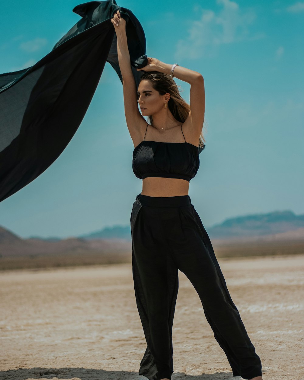 woman in black brassiere and black pants holding black textile on beach during daytime