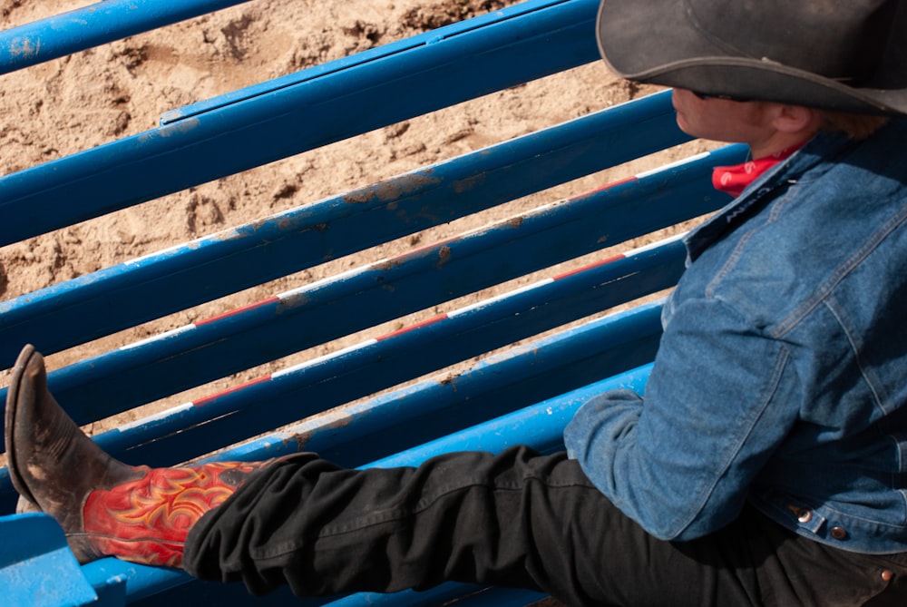 man in black jacket and black cap sitting on blue bench