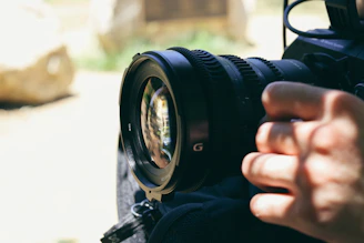 Close-up of a photographer adjusting a lens, with soft off-white background and charcoal shadows.