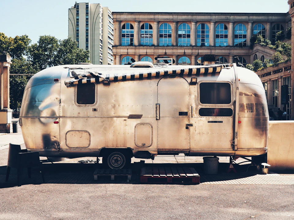 Vintage silver trailer parked on a street with black stripe and reflective windows behind