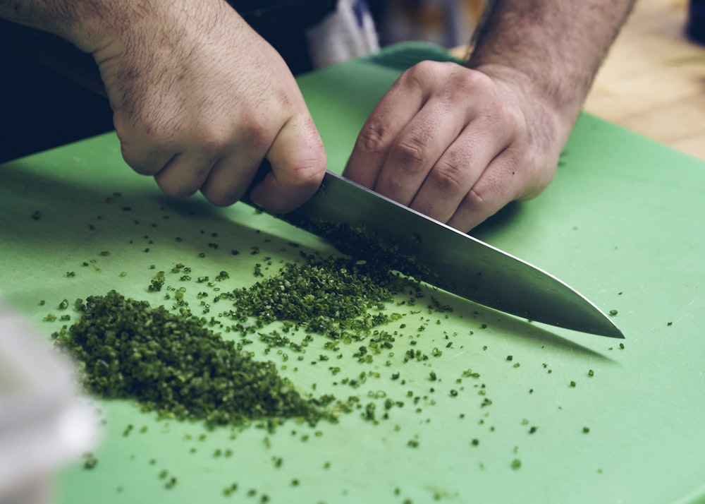 person slicing green vegetable on green chopping board