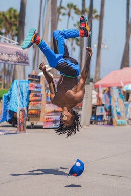 sports photography,how to photograph man doing a backflip on the venice boardwalk in california; man in blue pants and black tank top doing hand stand during daytime