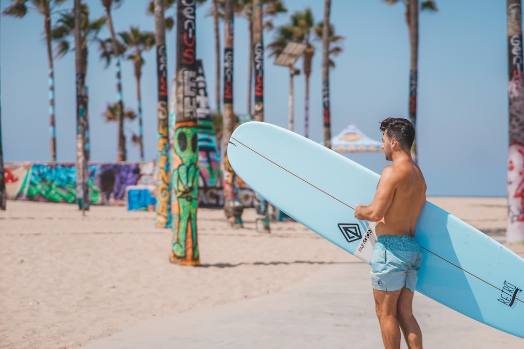topless man in blue denim shorts holding white surfboard during daytime