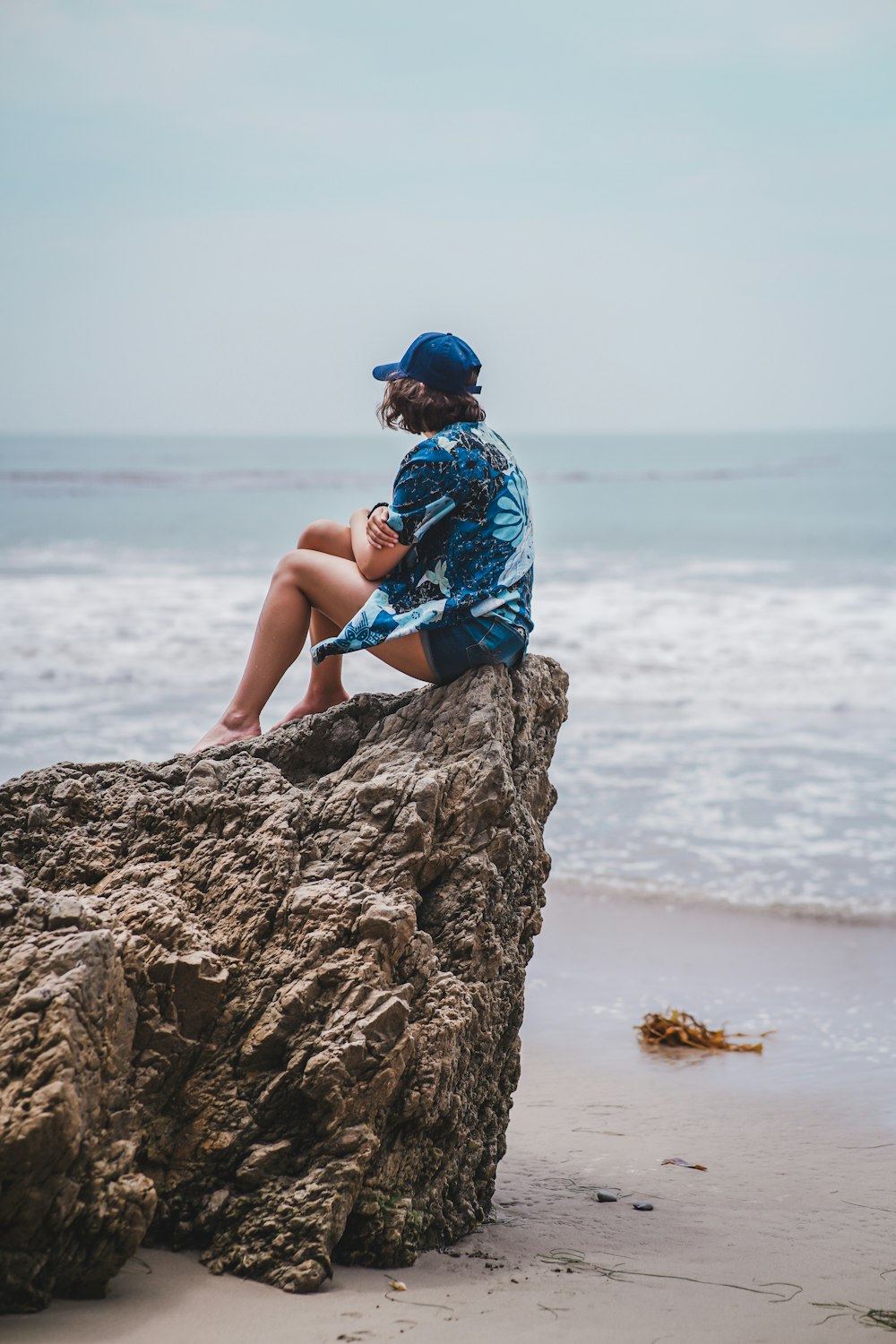 woman in blue and white floral dress sitting on rock near sea during daytime