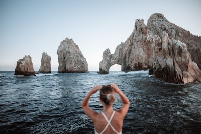 woman in white bikini on body of water near brown rock formation during daytime