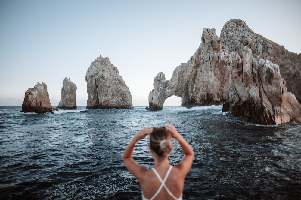 woman in white bikini on body of water near brown rock formation during daytime