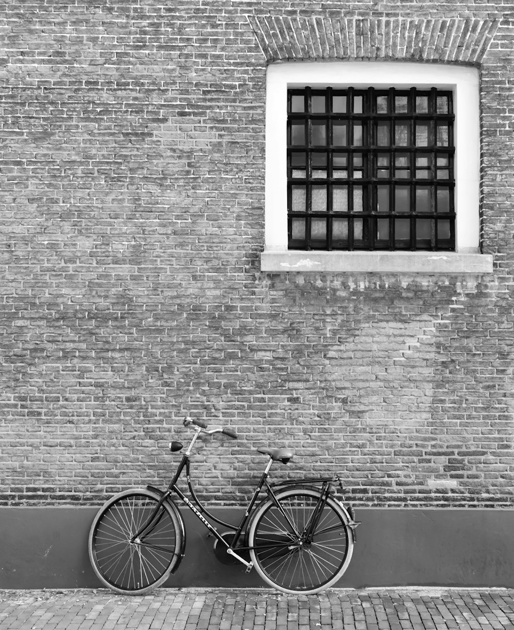grayscale photo of city bike parked beside brick wall