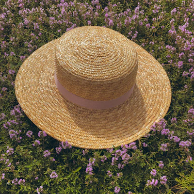 A colorful, patterned sun hat hanging on a rustic wooden fence surrounded by blooming flowers.