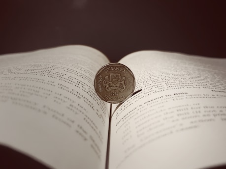 An illustrated open book with coins and children gathered around, symbolizing stories about money.