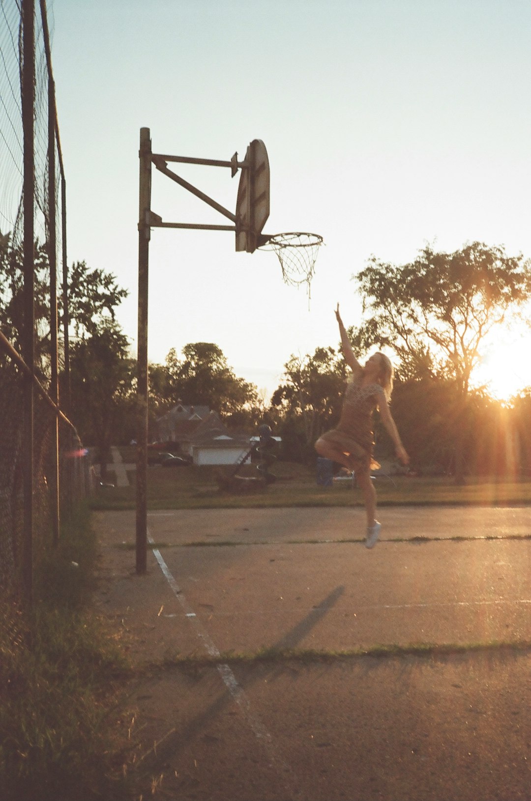 woman in white tank top and black shorts jumping on basketball hoop during sunset