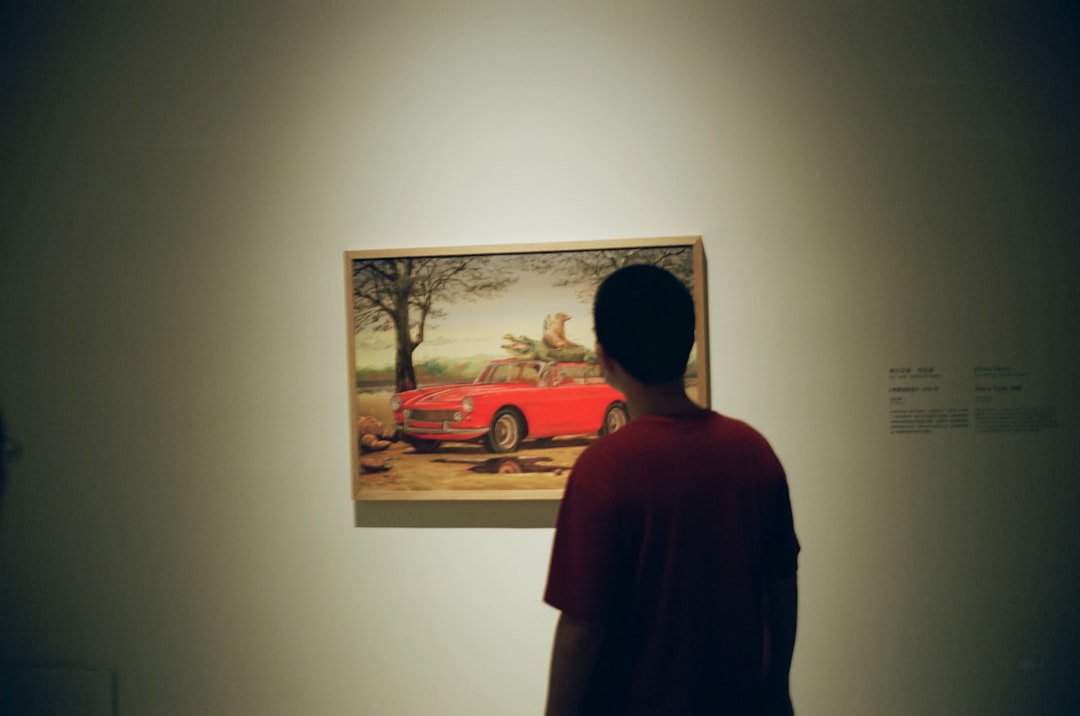 man in red shirt standing near body of water painting