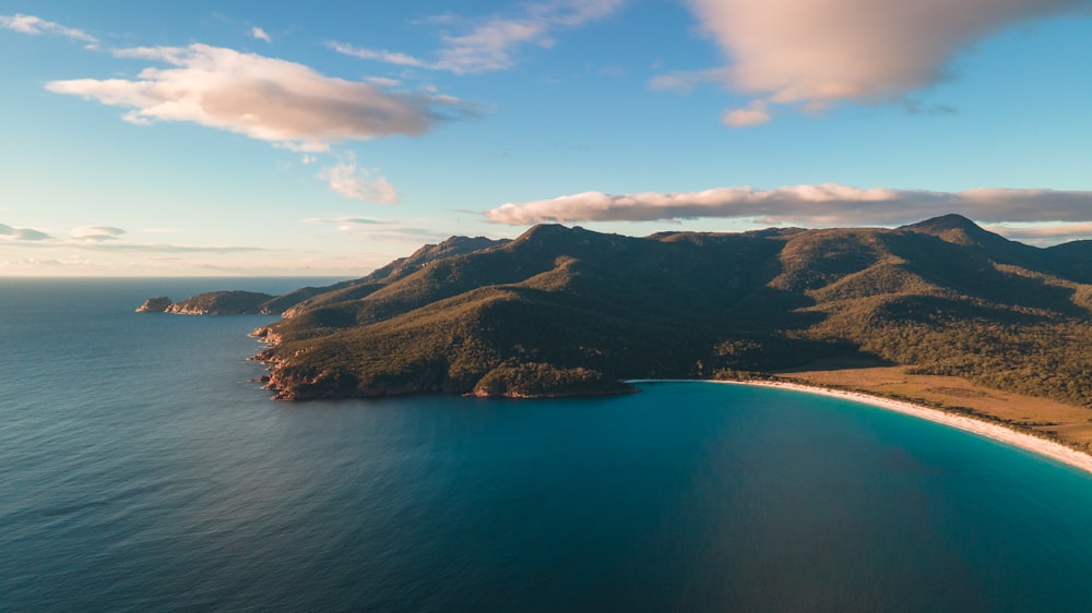 green and brown mountain beside blue sea under blue sky during daytime