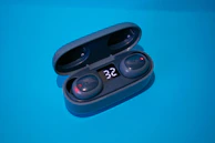 A compact wireless earbud case open to reveal earbuds with glowing LED indicators.