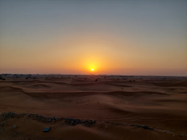 A warm sunset over the Egyptian desert with a motorcycle trail winding through sand dunes.