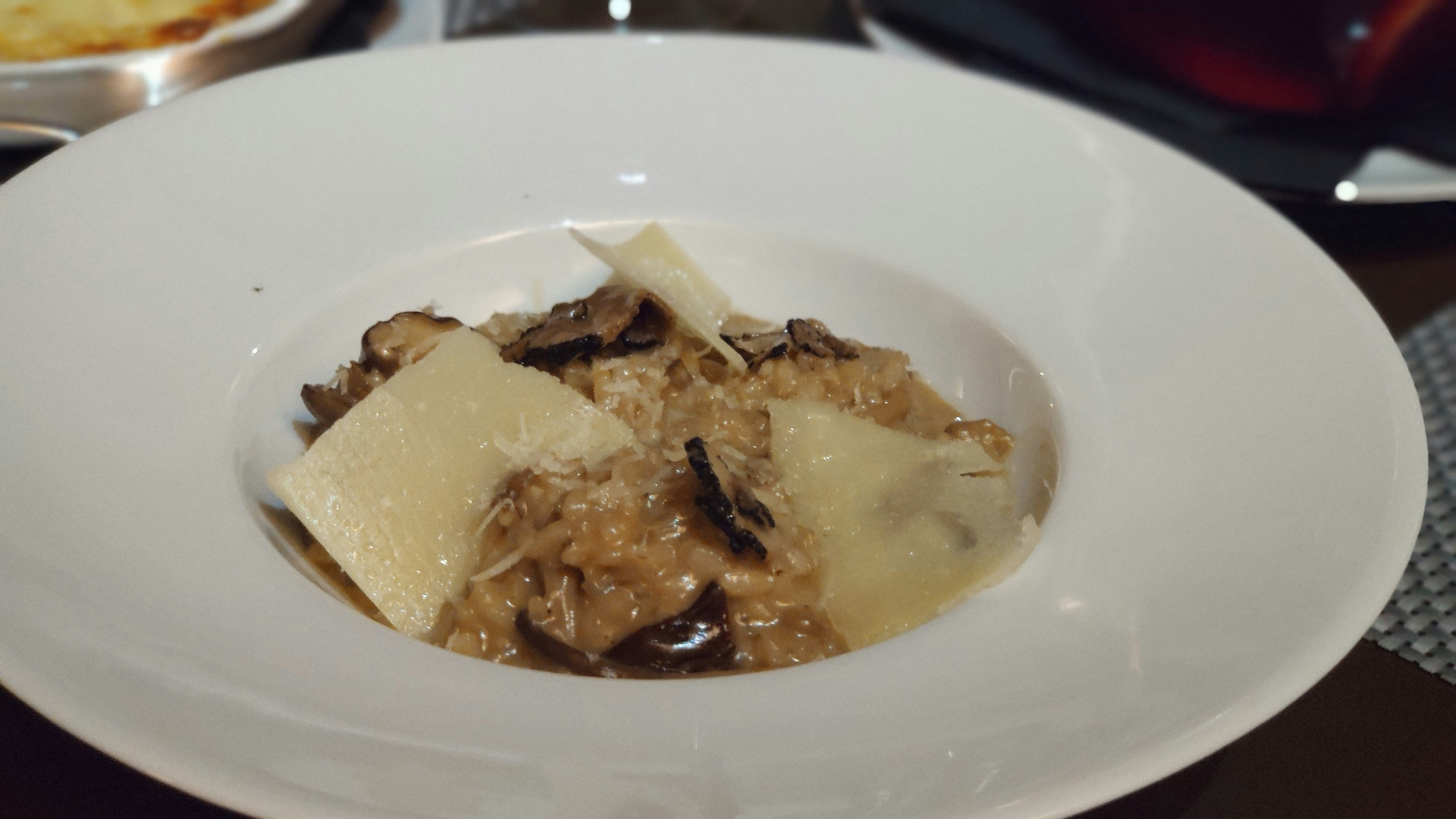 Creamy risotto in a white bowl with fresh herbs and shaved cheese in bright natural kitchen light