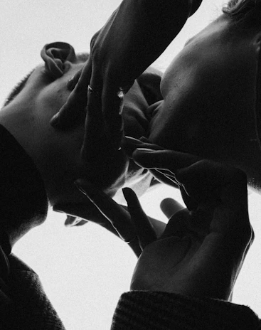 An intimate black charcoal-toned portrait of a couple holding hands, shadows playing softly on their faces.