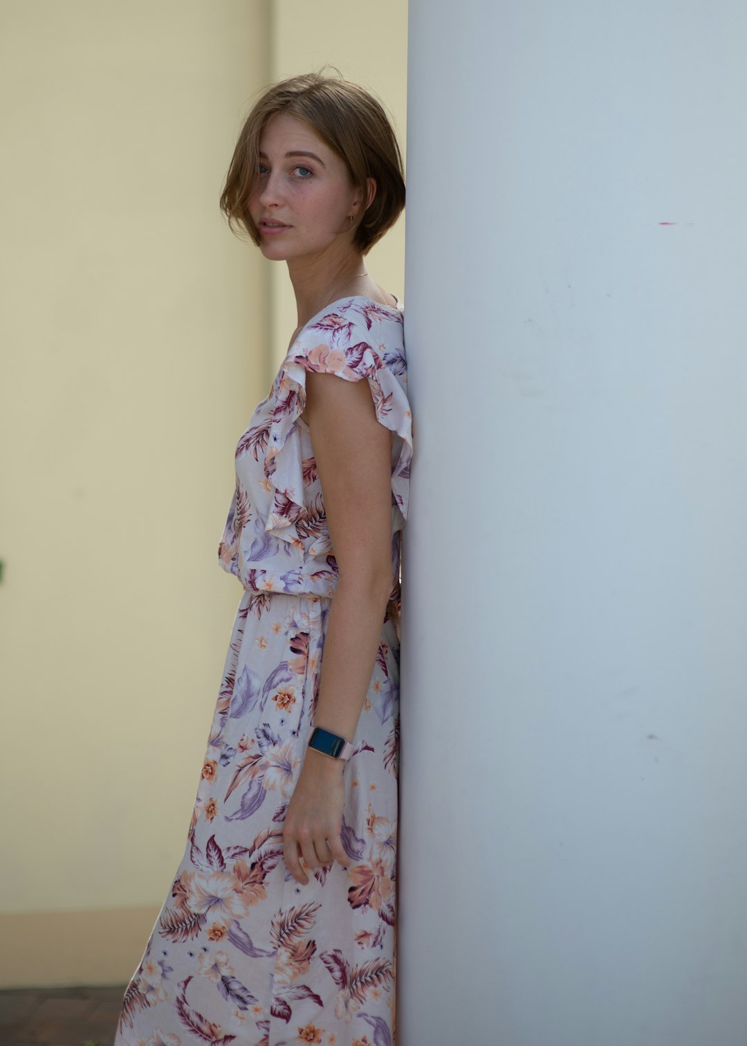 girl in white pink and blue floral dress standing beside white wall
