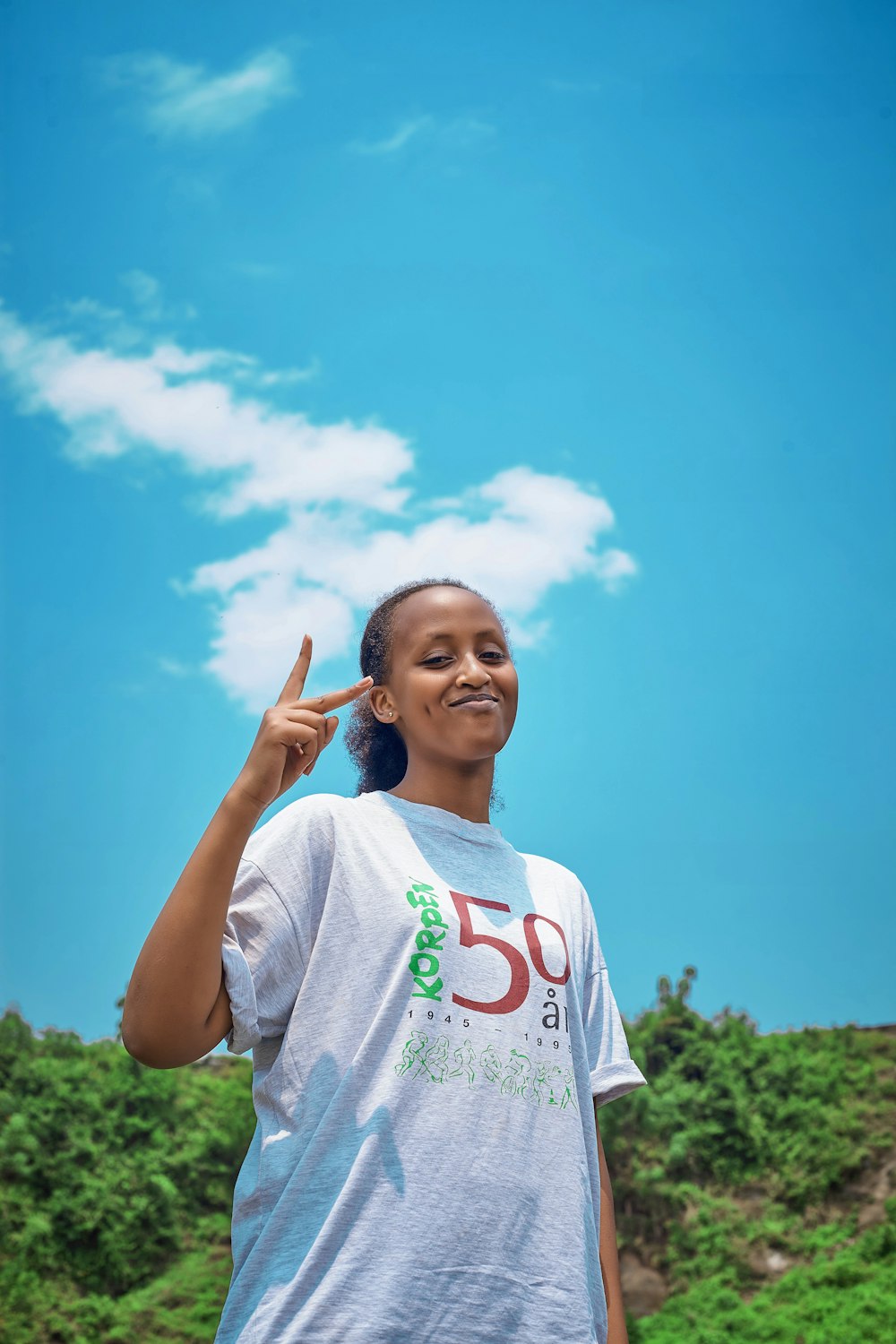 girl in white crew neck t-shirt standing on green grass field under blue sky during