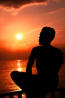 A serene moment of a person sitting peacefully by a calm lake at sunset, embodying presence and calm.