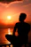 A serene image of a person sitting quietly by a calm lake at sunset, reflecting inwardly.