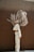 A person with braided hair is captured in motion, creating a dynamic silhouette against a plain, dark brown wall. Their outfit consists of a matching light-colored suit jacket and pants, revealing a confident and stylish demeanor.