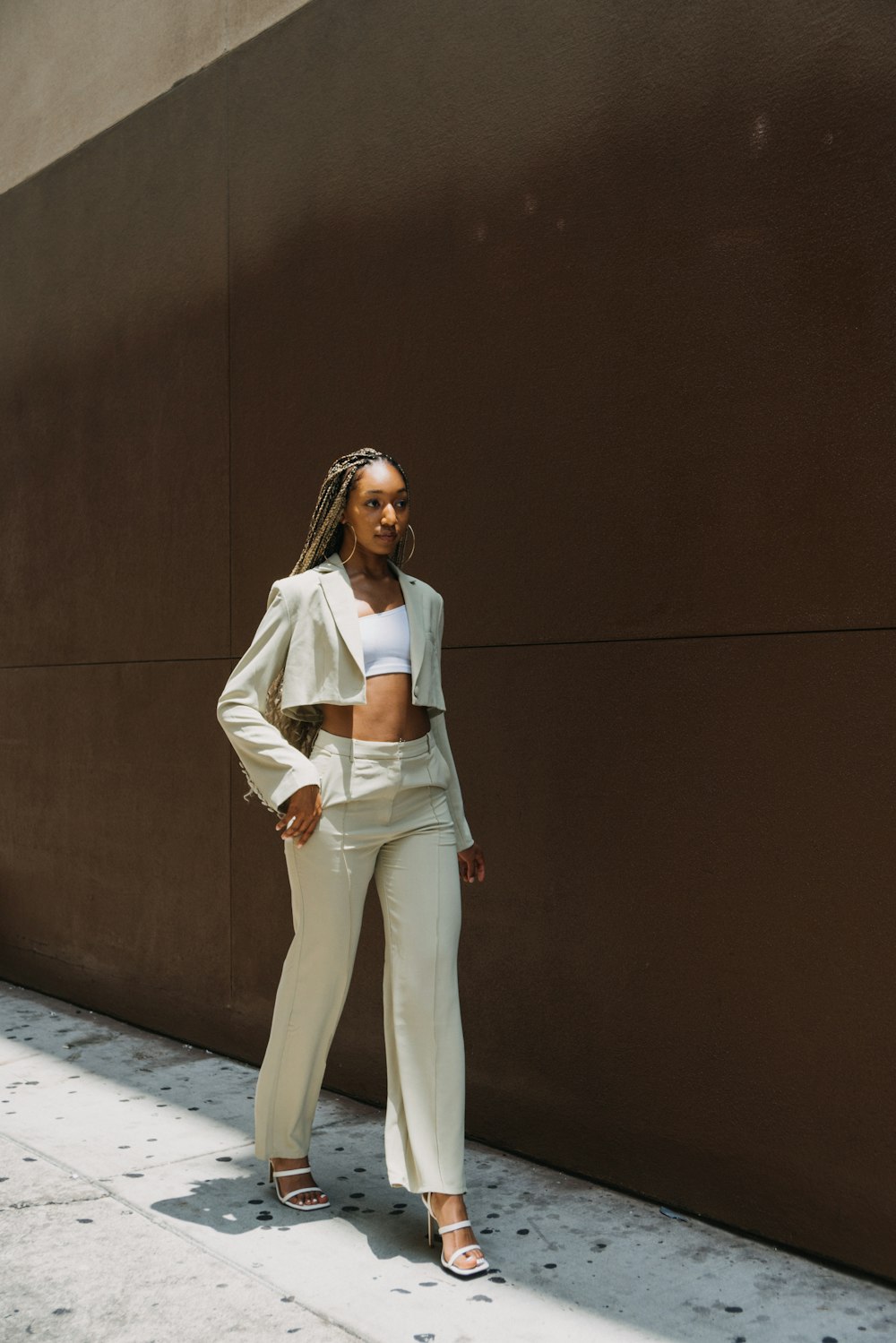 woman in white long sleeve shirt and white pants standing beside brown wall