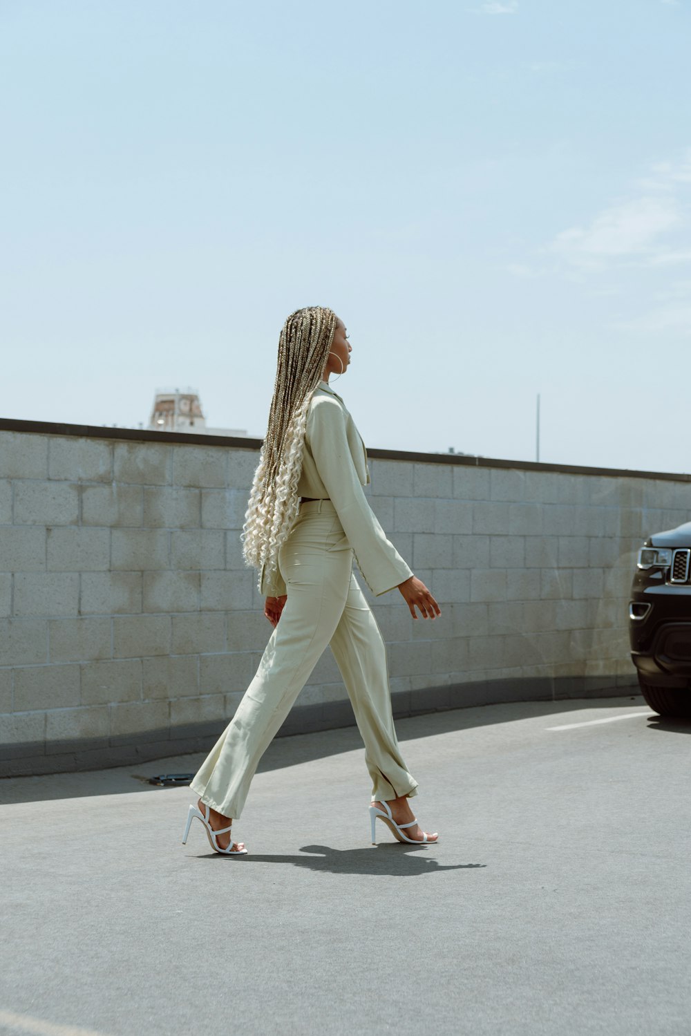 woman in white pants and white cardigan walking on sidewalk during daytime