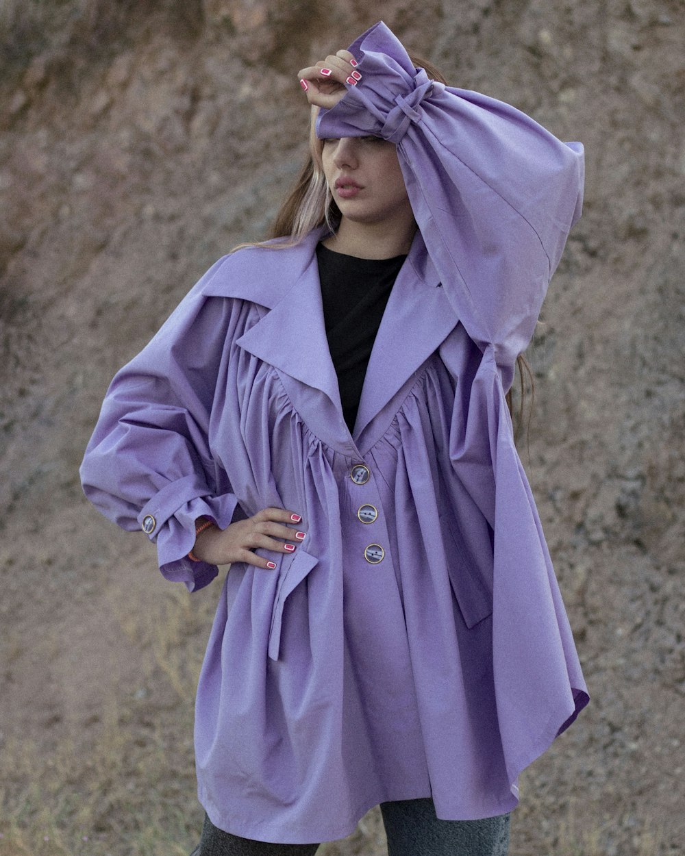 昼間、茶色の野原に立つ紫色のコートを着た女性