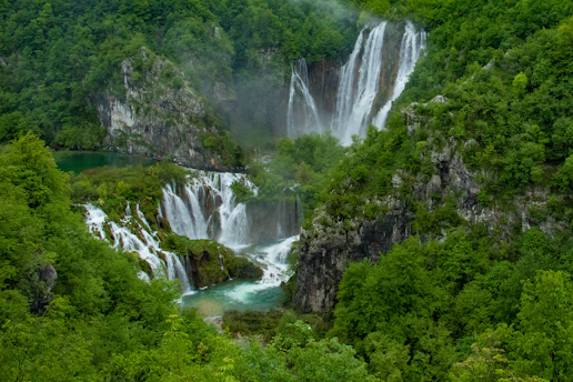A misty view of Sathodi Falls plunging into a clear pool, framed by dense forest foliage.