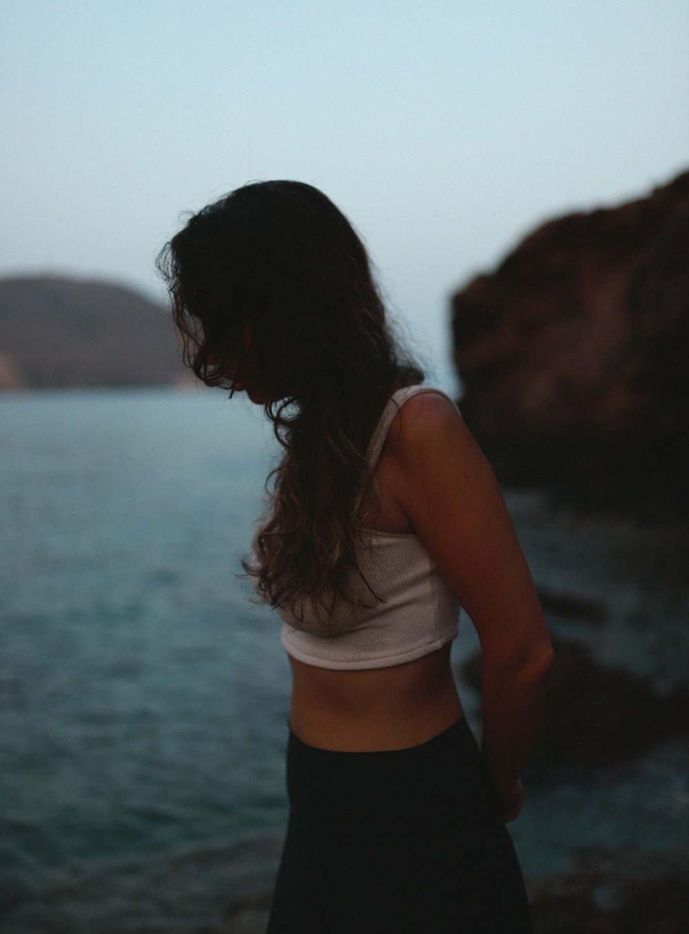 woman in white tank top and black shorts standing near body of water during daytime