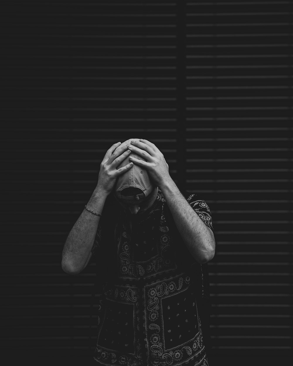 man in black and white floral shirt covering face with his hands