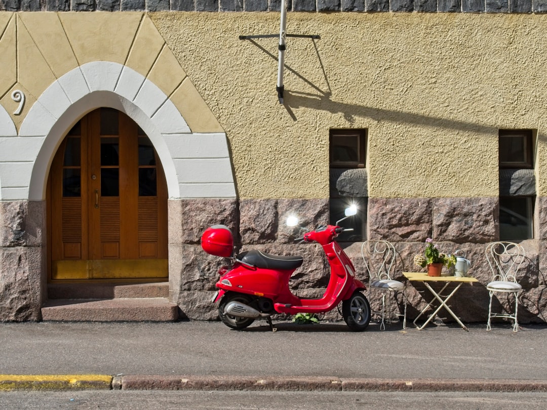 red motor scooter parked beside beige concrete building