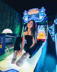 A person sitting on an arcade game machine platform with neon lights in the background. The arcade game is called 'Lane Master' and features a colorful design with bowling-themed imagery.