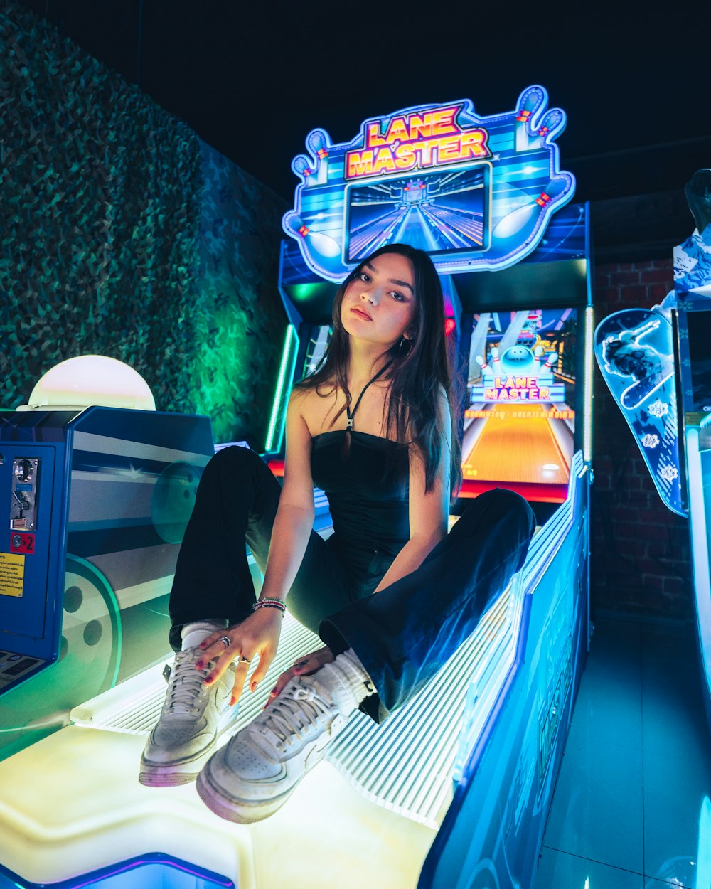 woman in black sleeveless dress sitting on blue and yellow arcade machine