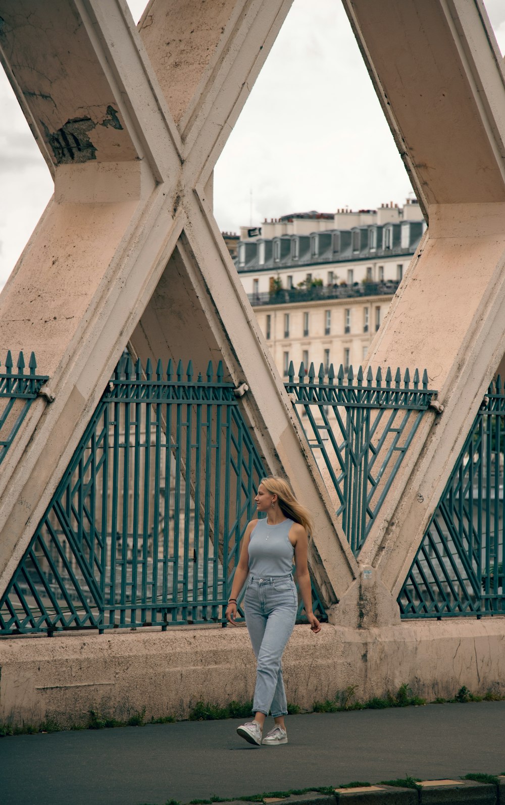 woman in white tank top and blue denim jeans standing on brown concrete bridge during daytime