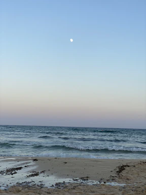 A sleek crepuson twilight surf Bluetooth speaker glowing softly on a sandy beach at dusk