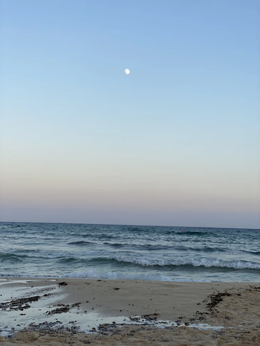 A sleek crepuson twilight surf Bluetooth speaker glowing softly on a sandy beach at dusk