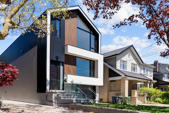 A modern house with black metal siding beside a traditional beige house