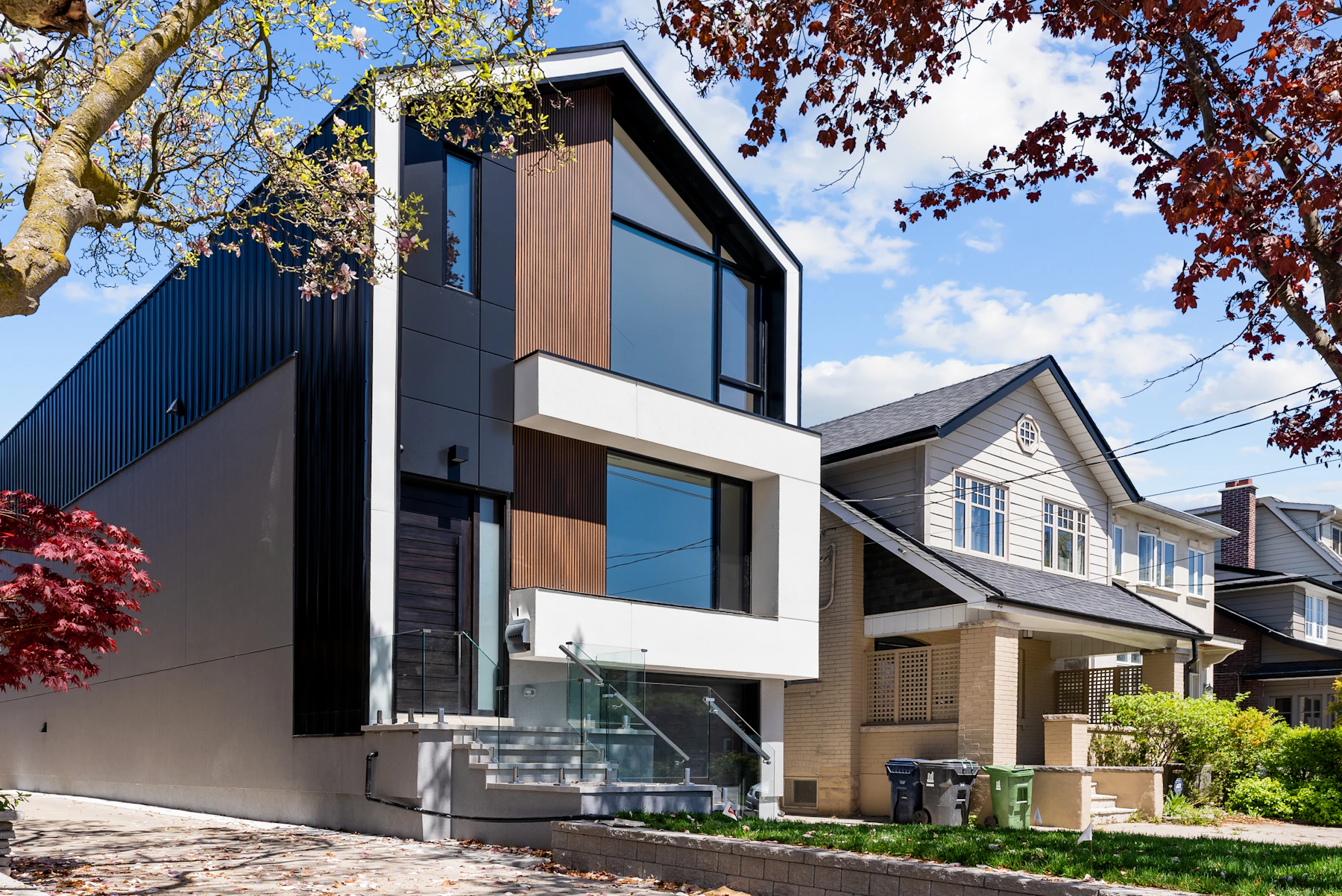 Striking modern renovated home with dark cladding beside a traditional house