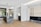 A modern kitchen with sleek, minimalist design featuring a large island with a marble countertop and built-in sink. The room has wooden flooring and neutral-colored cabinets, with a staircase leading to an upper floor. Large windows allow natural light to fill the space, enhancing its open and airy feel.