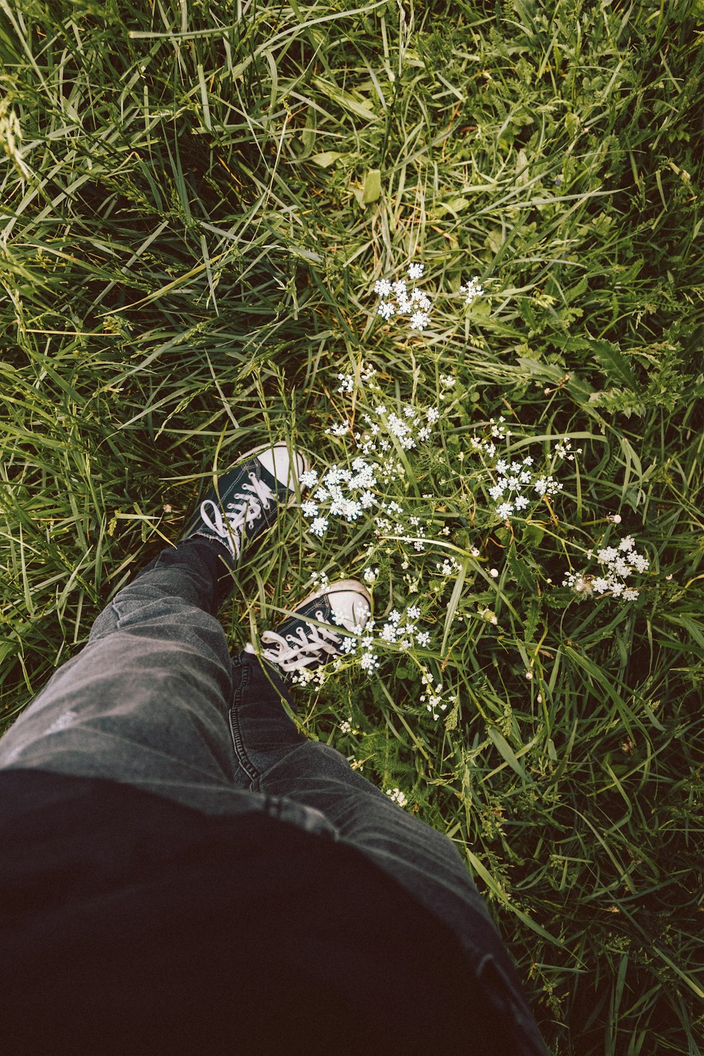 person in black pants and black and white sneakers standing on green grass field