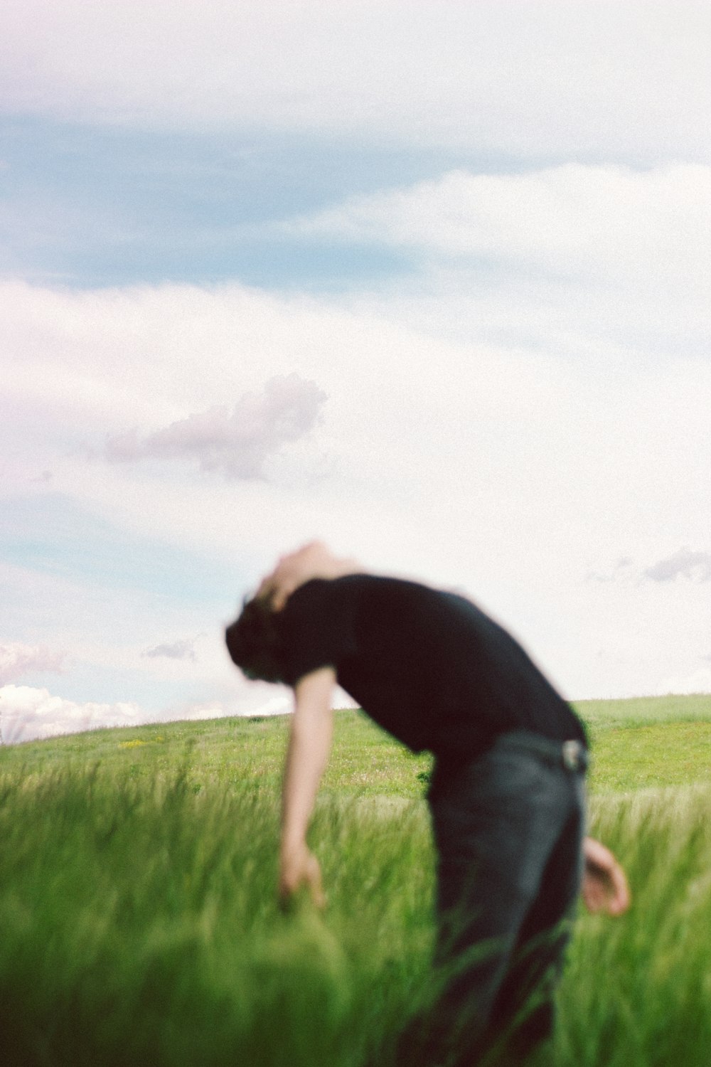 Uomo in t-shirt nera e jeans in denim grigio in piedi sul campo di erba verde durante il giorno