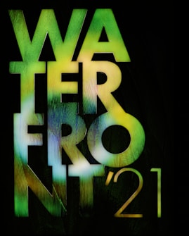 Large bold text spelling 'WATERFRONT '21' is displayed with a gradient of green and yellow colors against a black background. The text appears to have a textured design, resembling a natural pattern.