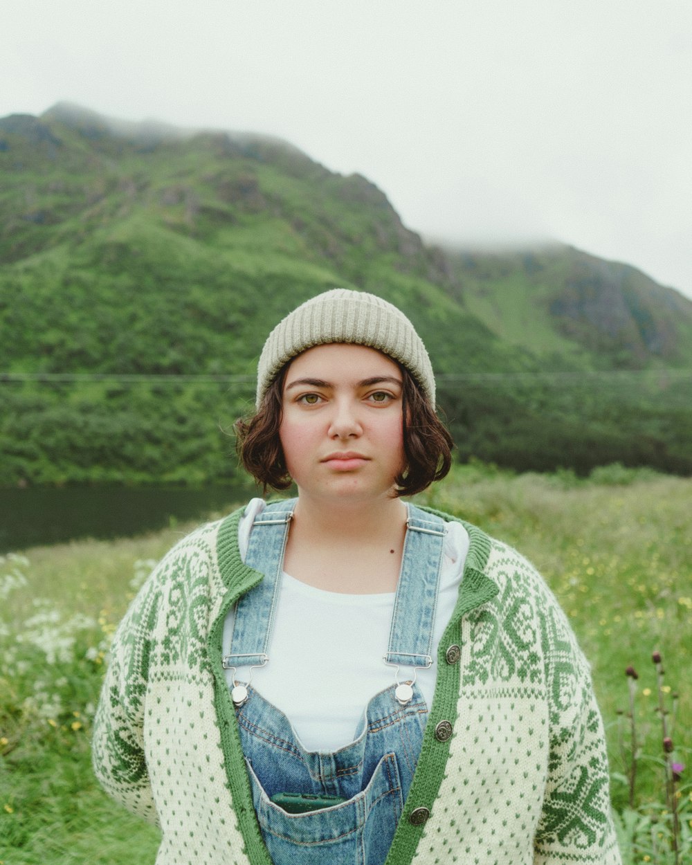 woman in white knit cap and green cardigan standing on green grass field during daytime