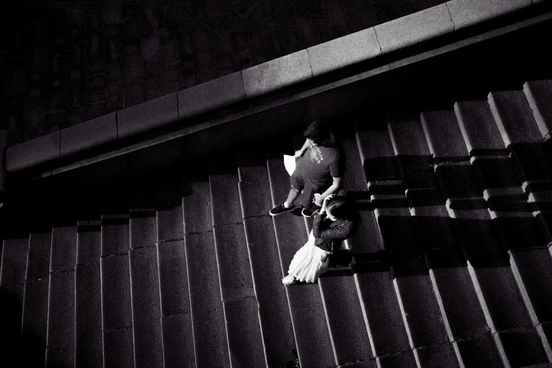 grayscale photo of man in white shirt and pants sitting on stairs