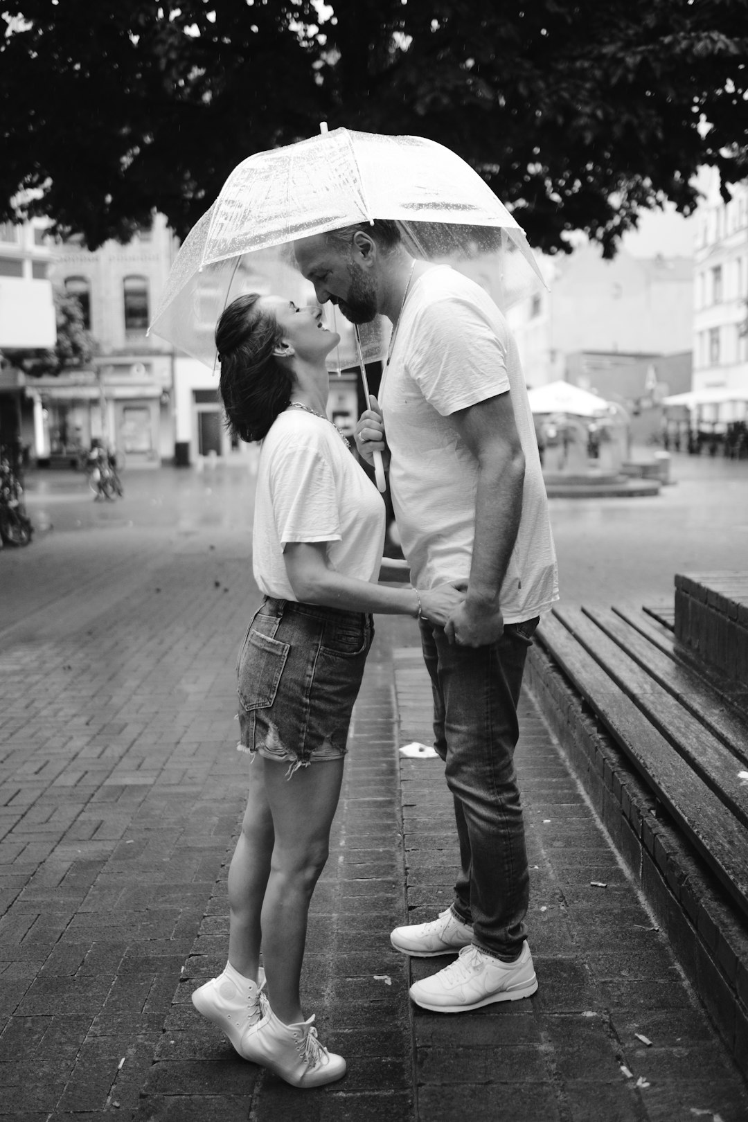 grayscale photo of man and woman holding umbrella walking on sidewalk