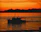 Boat gliding near waterfalls at sunset with vibrant orange sky.