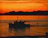 Boat gliding near waterfalls at sunset with vibrant orange sky.
